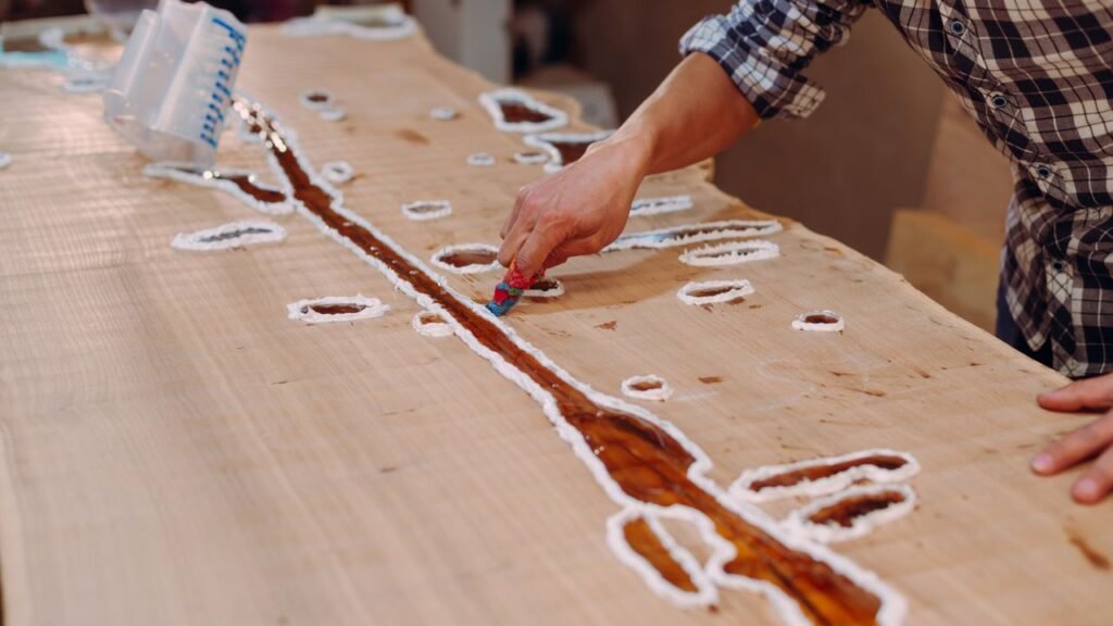 Craftsman filling knots and cracks in a live edge wood slab with clear epoxy resin