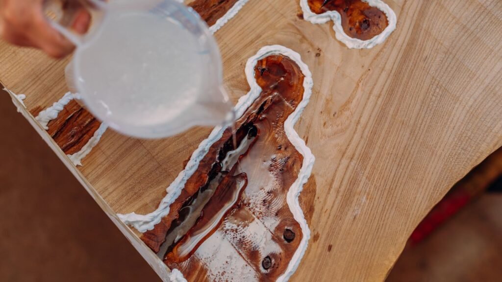 Close-up of clear epoxy resin being poured into wood cracks and knots taped off with painter's tape