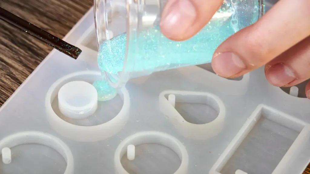 Pouring glitter-infused epoxy resin into a silicone mold for handmade jewelry