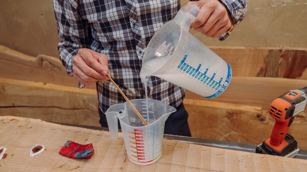Woodworker measuring and mixing epoxy resin and hardener at correct ratio in plastic measuring cups
