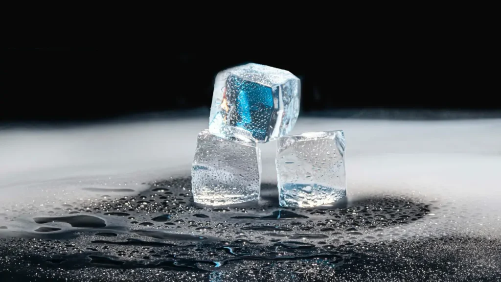 Three ice cubes on a dark, water-splashed surface, representing the freeze method for resin removal
