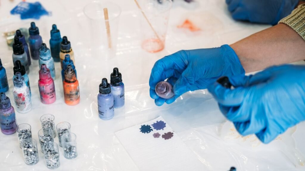 Gloved hands mixing purple mica pigment powder into epoxy resin with color swatch samples