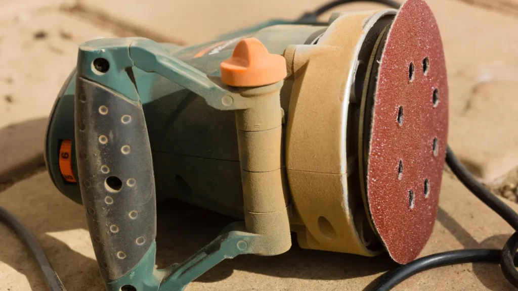 Orbital power sander with a sandpaper disc attached, used for sanding away cured resin from metal surfaces