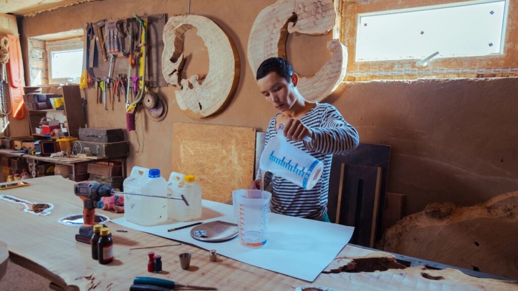 Woodworker pouring measured epoxy resin mixture into a container in his shop