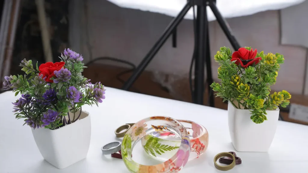 Handmade resin bracelets and rings containing pressed flowers, displayed next to artificial plants

