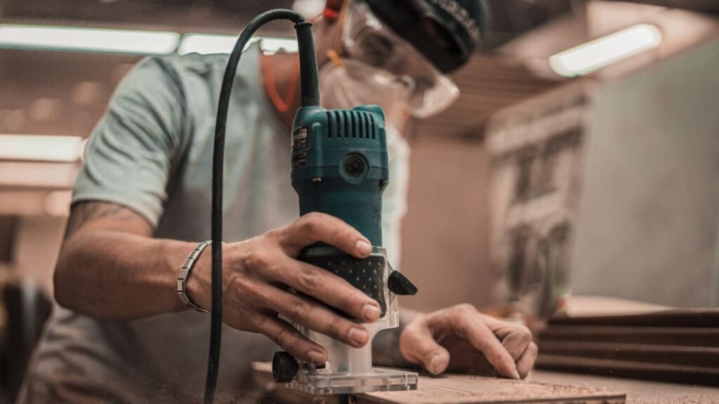 Woodworker using a hand router to trim excess cured epoxy resin from a wood slab edge