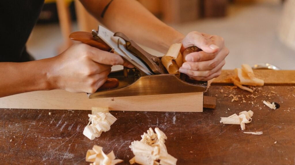 Hand plane smoothing raw wood surface with curled shavings before epoxy resin application